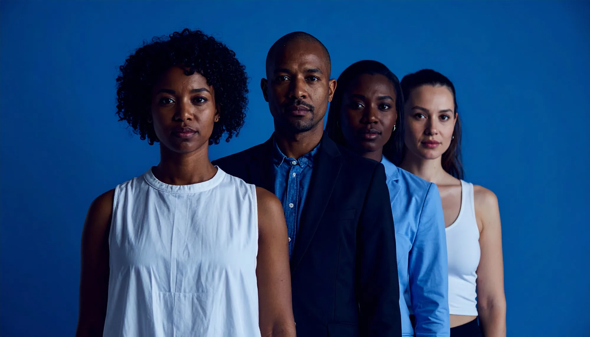 Four people standing one behind another against a deep blue backdrop